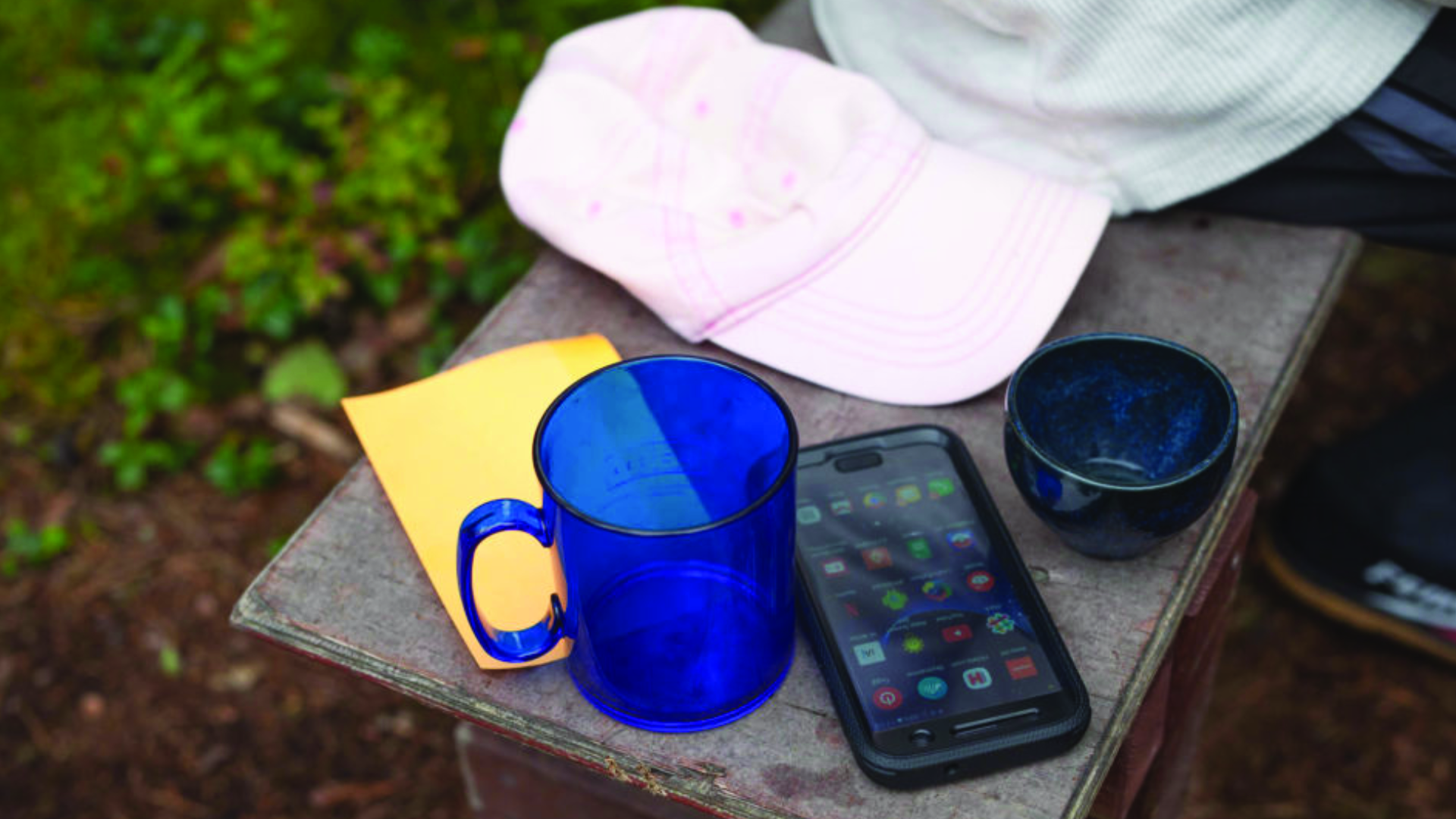 a cap with a plastic cup and a smartphone on a bench photo credit by Maija Savolainen
