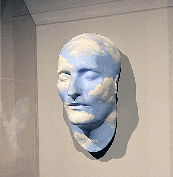 Plaster sculpture of a human face with sky superimposed on it.