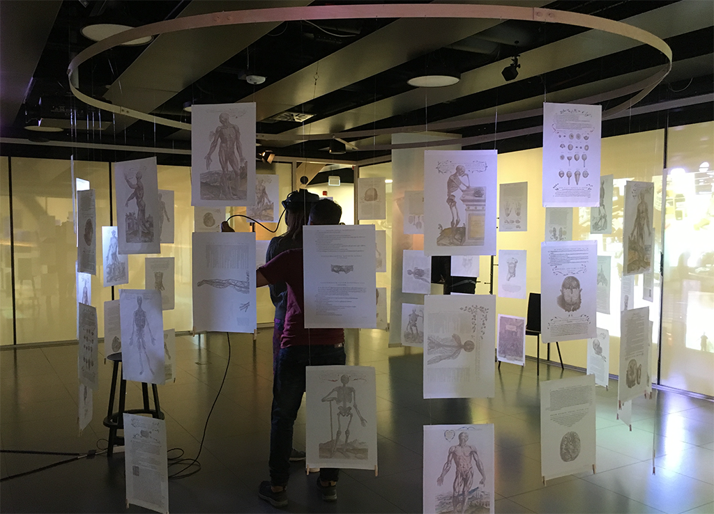 Virtual reality installation with pages from Vesalius' Anatomy Handbook printed on vellum suspended from ceiling by wood ring